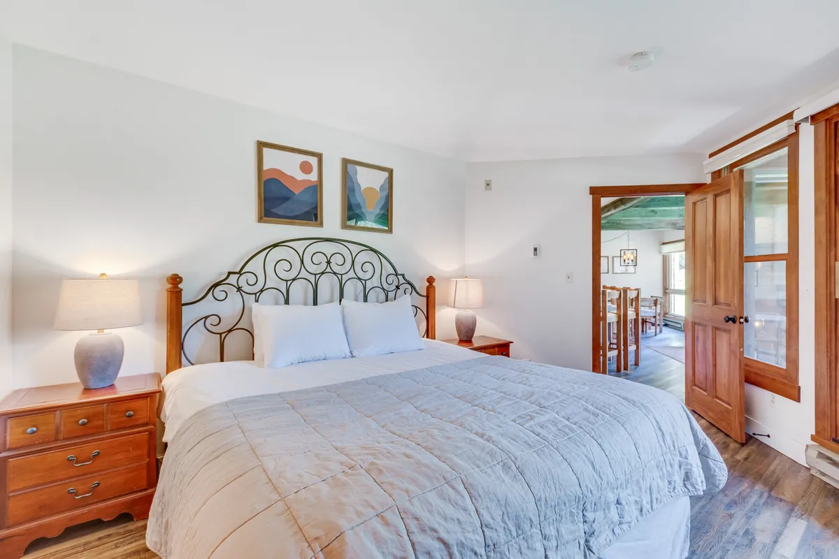 A tranquil bedroom scene featuring a bed with a decorative headboard, soft bedding, nightstands with lamps, and tasteful artwork on the walls. Natural light filters in, creating a restful atmosphere perfect for relaxation and rejuvenation.