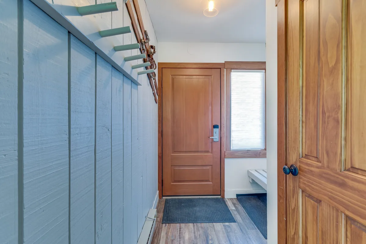 This image features a welcoming entryway with a wooden door, coat hooks, a sturdy bench, and a textured wall. The setting evokes the moment of arrival, offering space for guests to hang coats and take off shoes, immediately illustrating the 'gear-up' function described in the section.