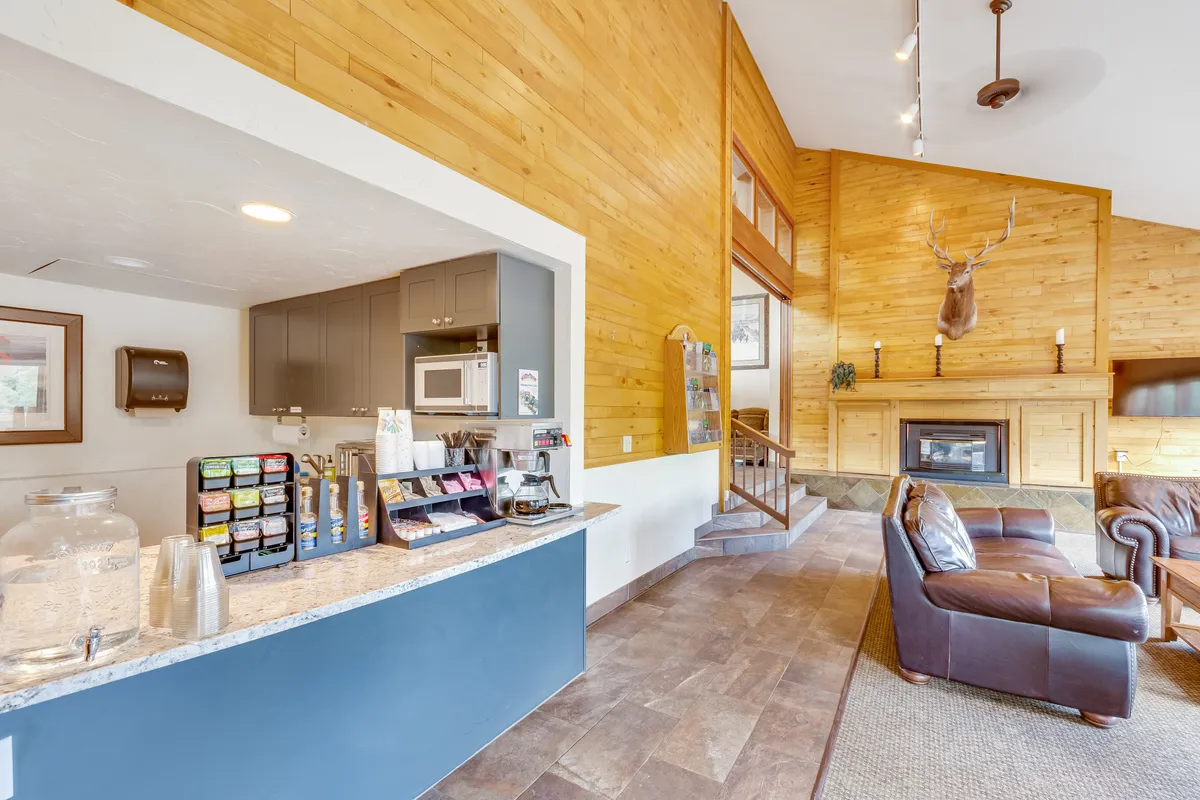 A cozy reception area features a front desk, plush sofa, fireplace, and wooden walls. The space is welcoming and hints at attentive guest services.