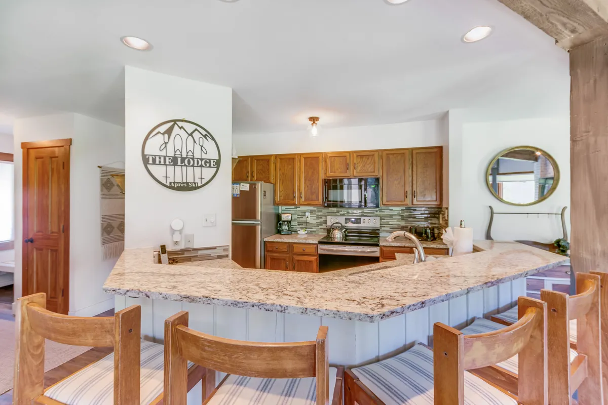 A functional kitchen area with granite countertops, wooden cabinets, modern appliances, and bar stools, accented by a 'Lodge' sign. The layout is perfect for cooking, sipping coffee, or socializing around the kitchen island.