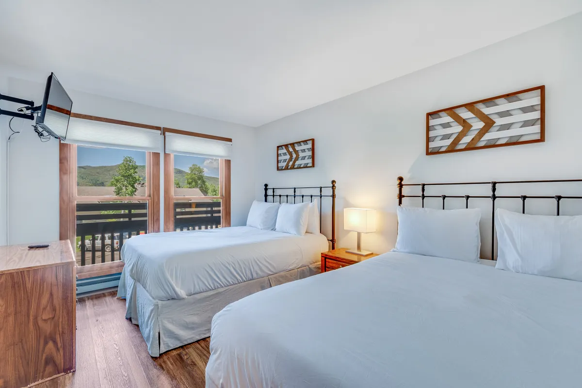 A comfortable bedroom with two beds, large windows offering scenic views, decorative wall art, and a TV. The room feels spacious and inviting, suitable for children, friends, or extra guests, and fosters a sense of shared comfort.