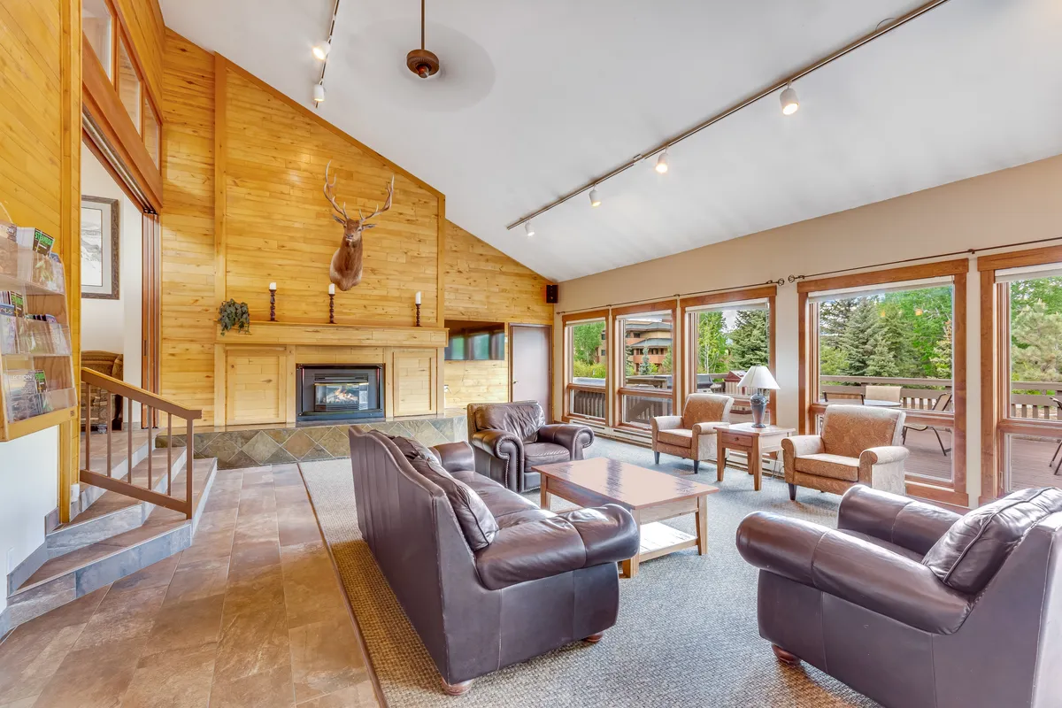 A cozy living area featuring a fireplace, large windows, and comfortable seating surrounded by wooden paneling. The windows provide glimpses of the outdoor environment, and the atmosphere invites guests to enjoy the warmth inside while remaining connected to the natural beauty outside.