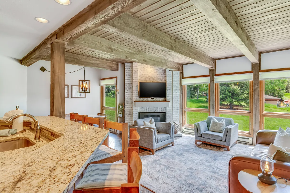 The image showcases the condo's inviting living area with a sleek granite countertop, a glowing fireplace, plush seating, and expansive windows framing mountain views. The space is filled with natural light and designed for relaxation, conversation, and enjoying sunsets over Steamboat Springs.