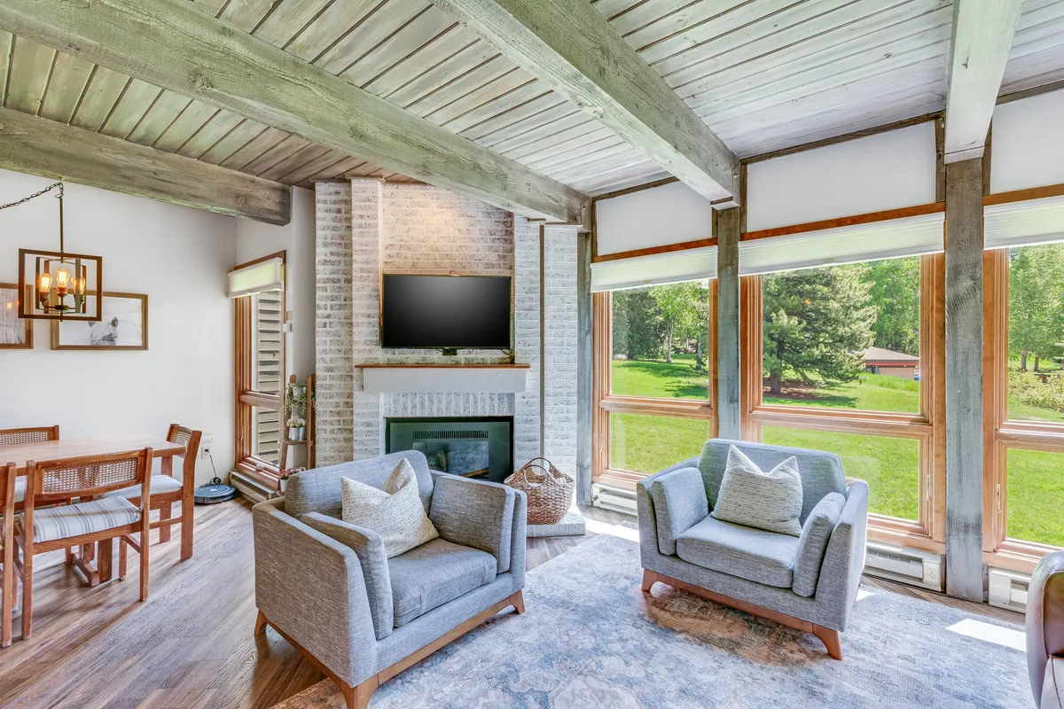 This inviting scene highlights comfortable seating arranged around a glowing fireplace with large windows providing natural light and views of the outdoors. The area is ideal for relaxing after a day outdoors or sharing stories with loved ones.