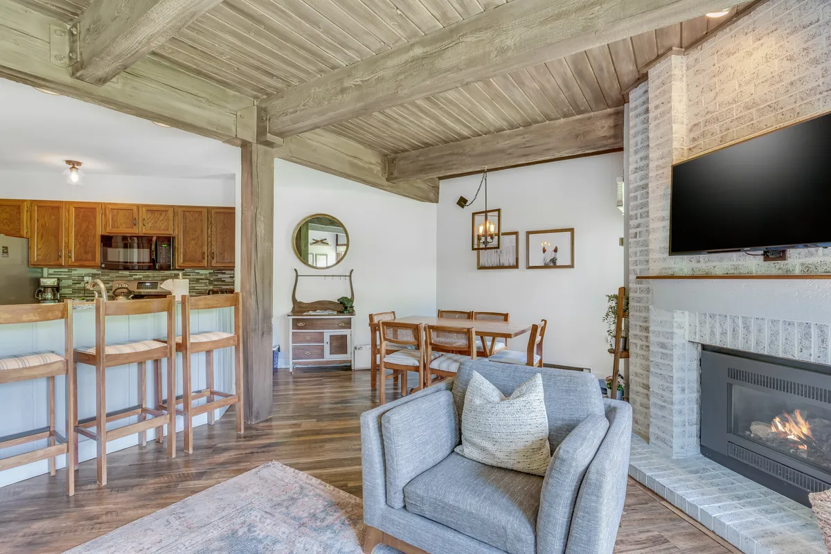 This image captures the open-concept living, dining, and kitchen area. It features a cozy fireplace as a focal point, a dining table ready for group meals, a kitchen bar area, a plush sofa, and a soft decorative mirror, all bathed in warm, ambient light. The layout encourages gatherings and togetherness, echoing the section's emphasis on shared experiences.