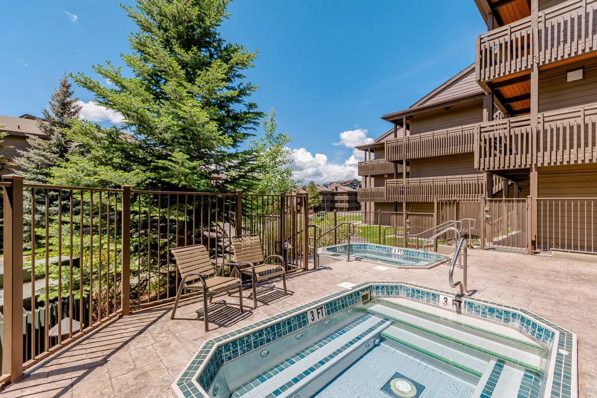 The scene showcases outdoor hot tubs set amidst lush greenery, with patio seating nearby for socializing and relaxation. The tranquil setting emphasizes both recreation and a social atmosphere.