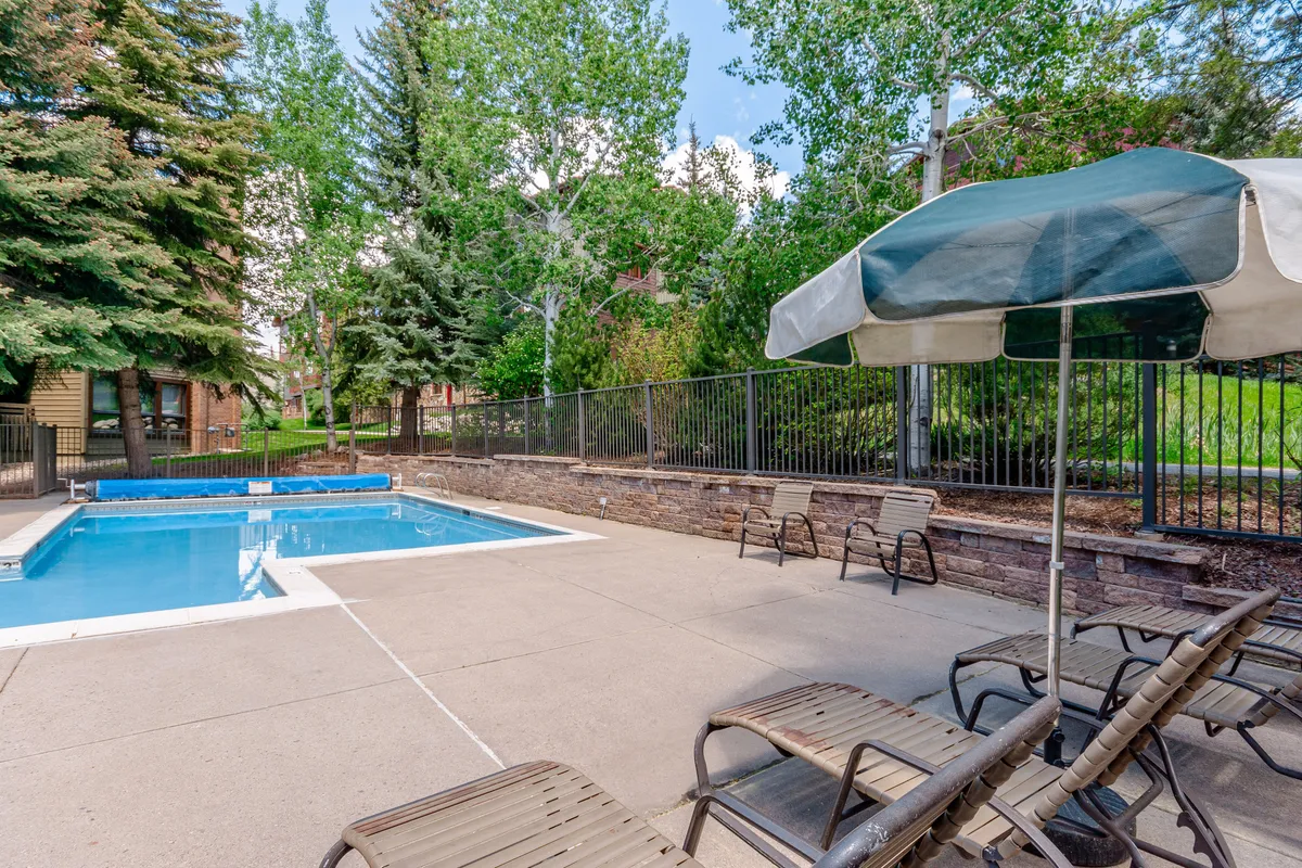 A second angle of the outdoor swimming pool, featuring several lounge chairs and a large patio umbrella. The composition emphasizes the poolside social experience, suggesting a lively setting for afternoon gatherings or quiet relaxation.