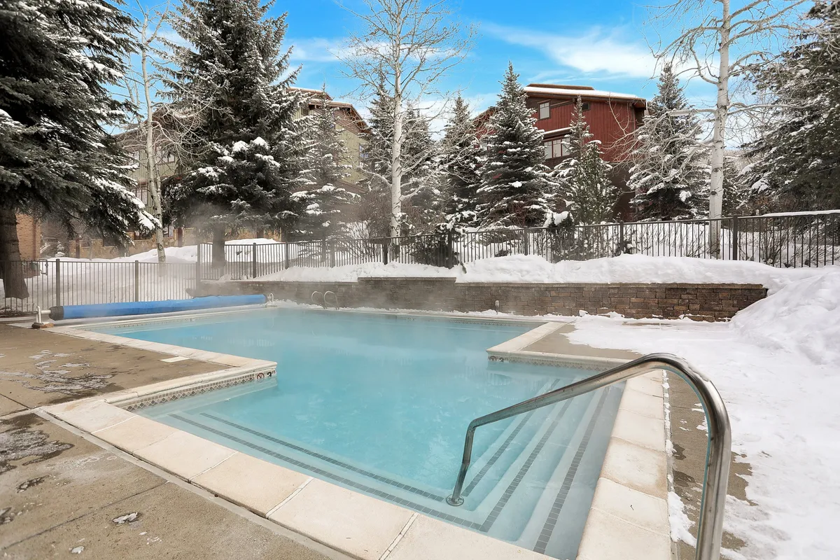 This image features a heated pool surrounded by snow-covered ground and trees, creating a striking contrast between the warm water and winter scenery. Lounge chairs are visible poolside, emphasizing a year-round resort atmosphere.